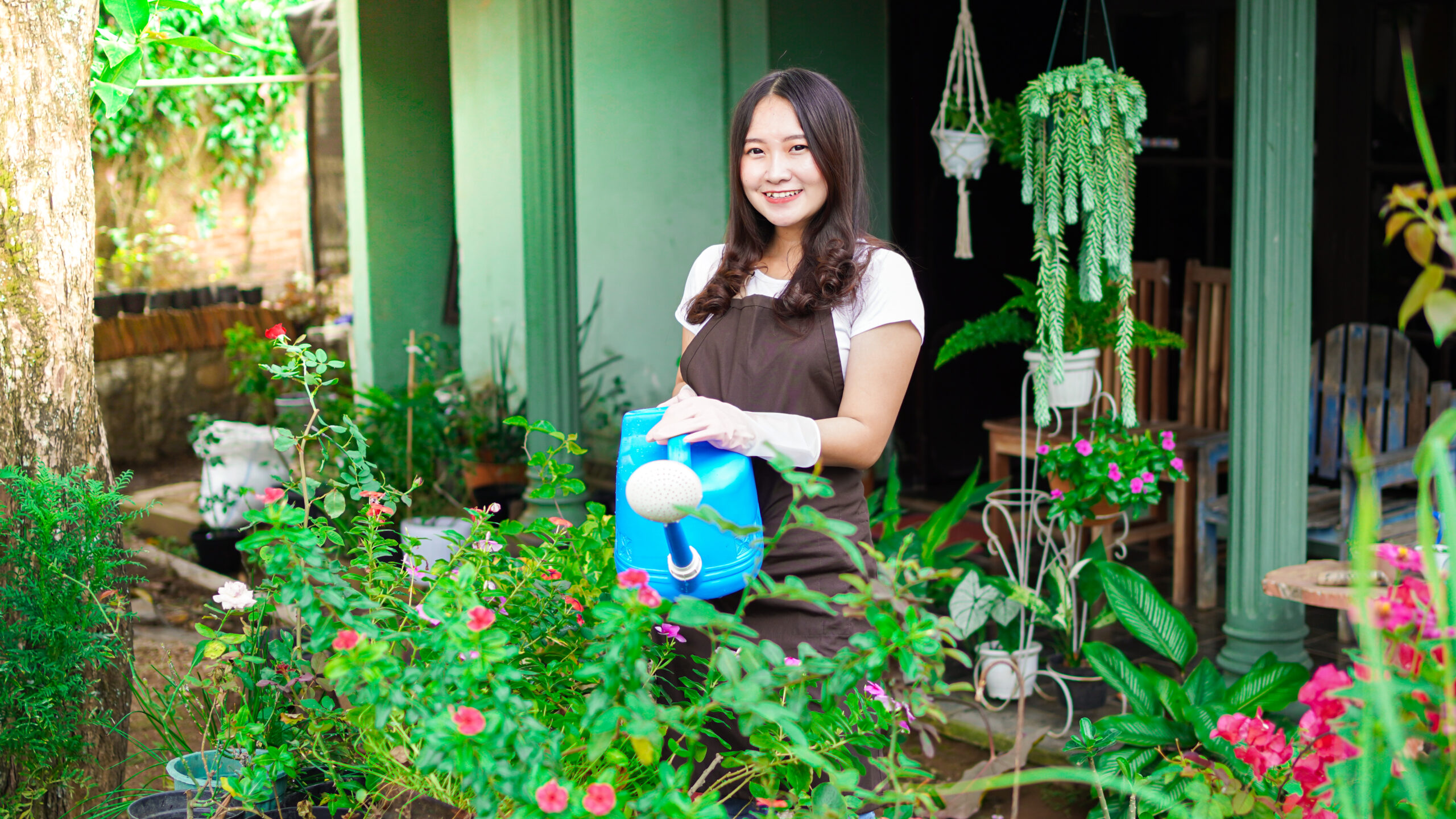 the asian woman is watering the flowers and plants at the garden